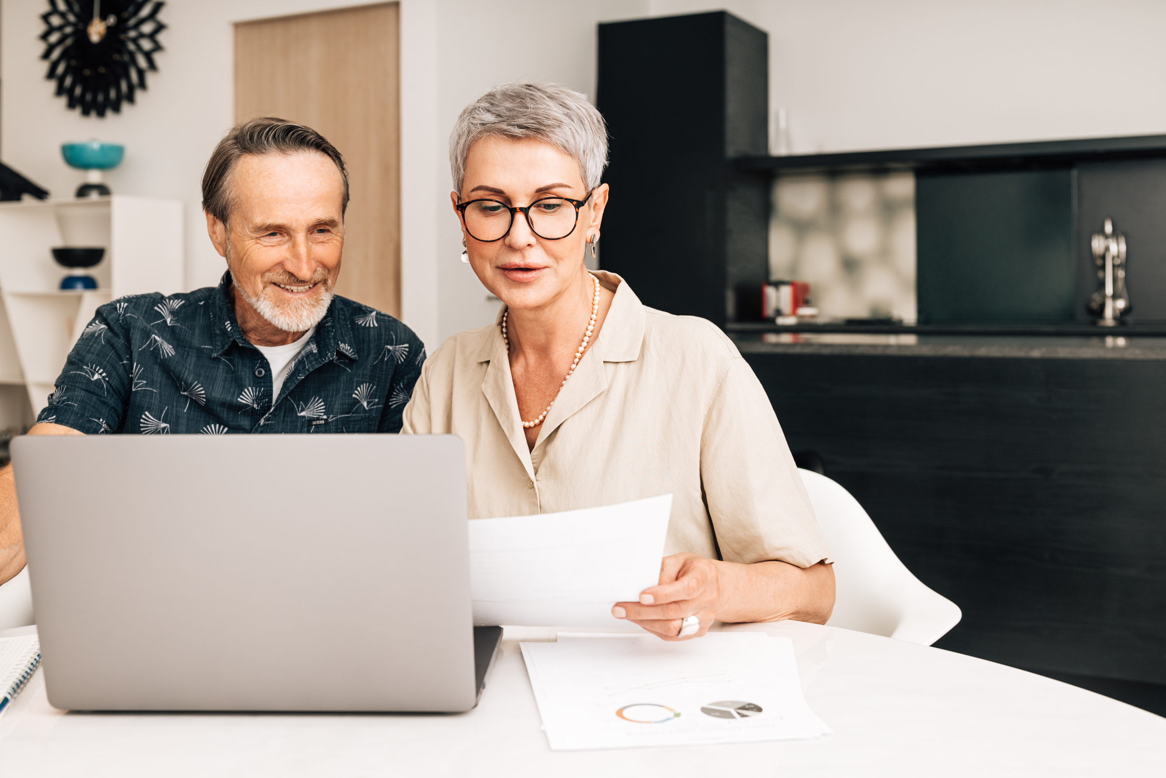 Older couple reviewing paperwork together at a laptop