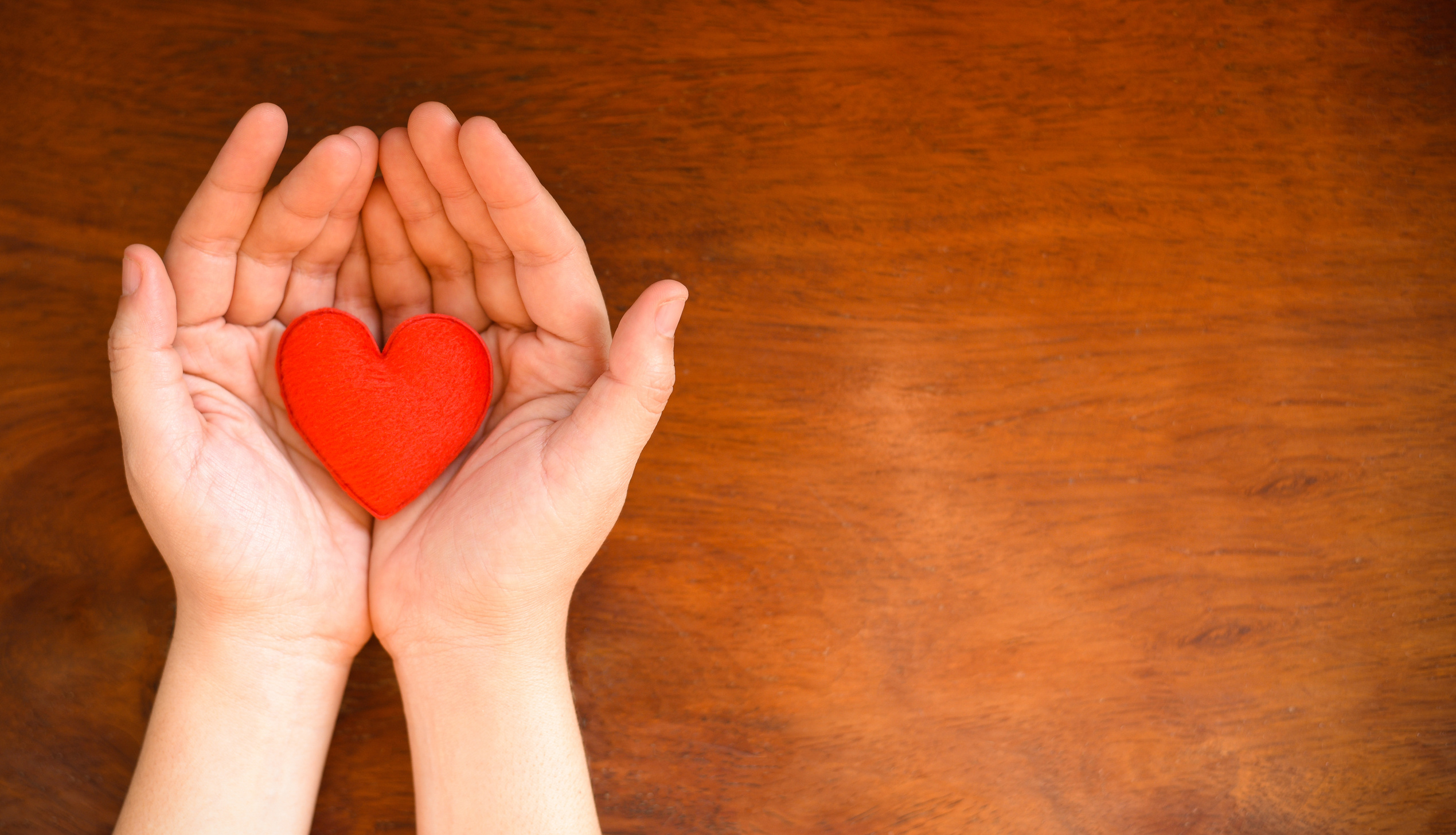 Two hands holding a small red heart